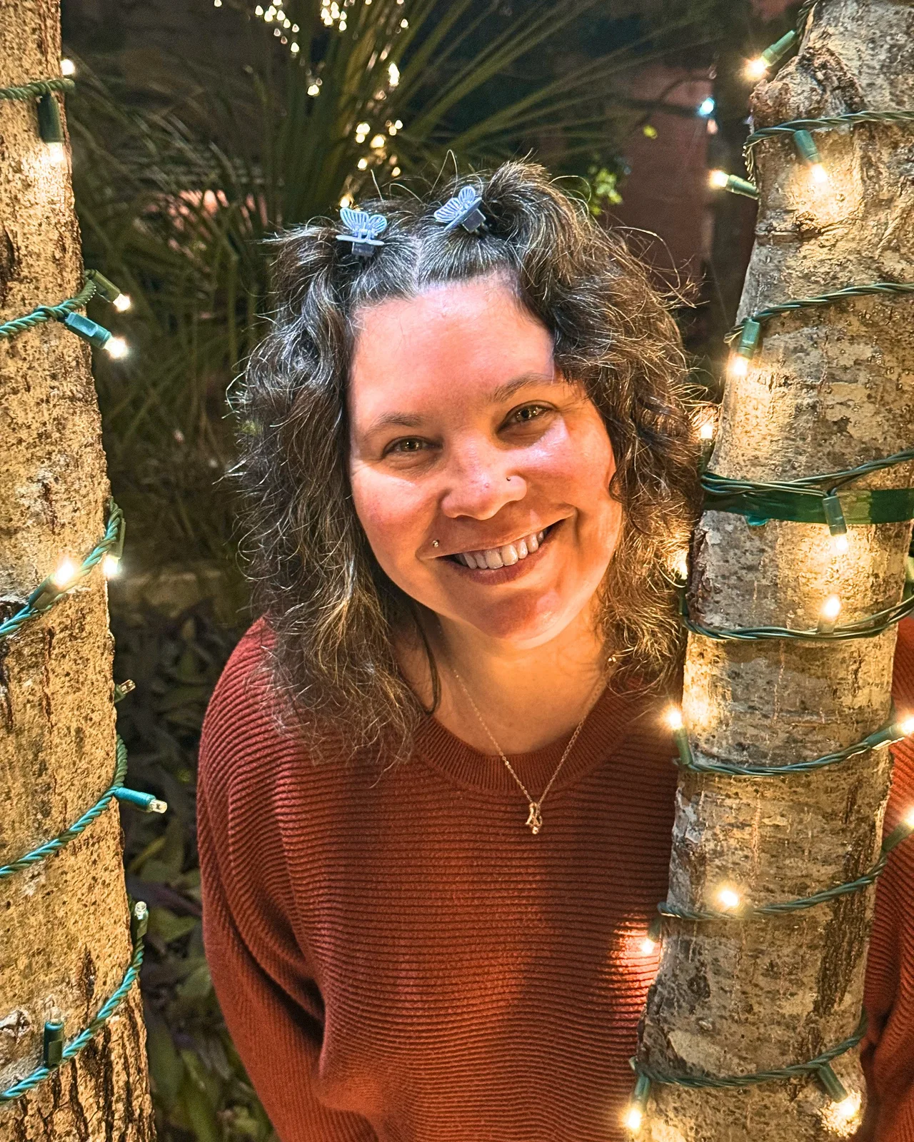 Naomi smiling between two trees wrapped in string lights